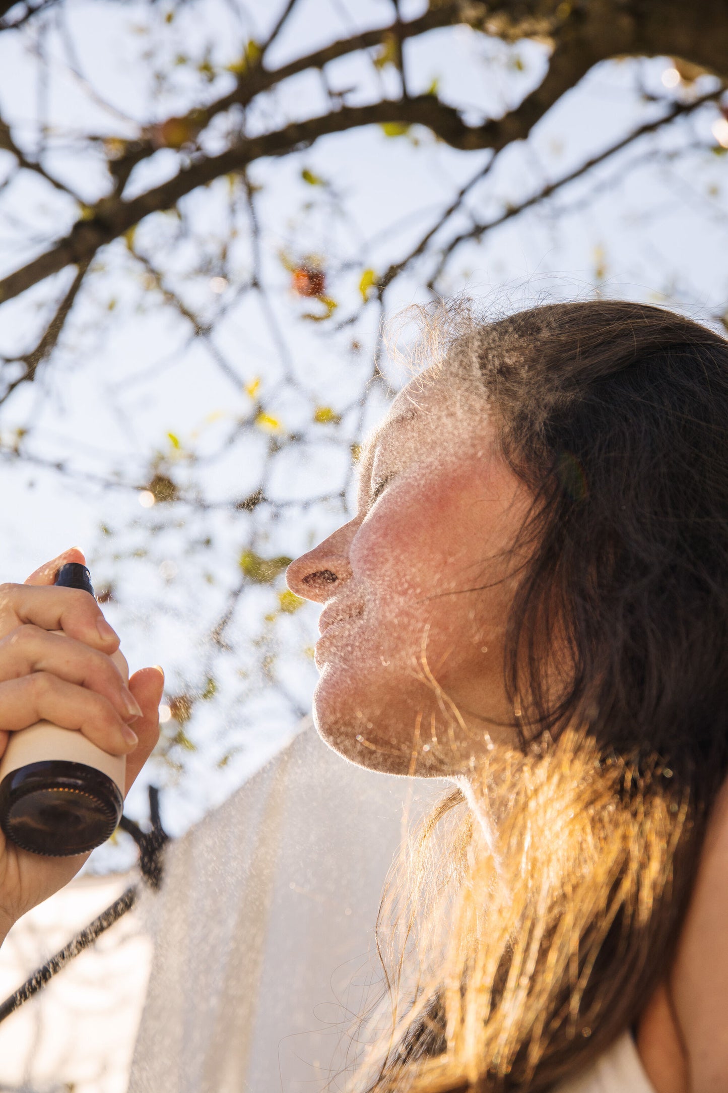 Woman spraying hydrating neroli mist on face outdoors for refreshing natural skincare