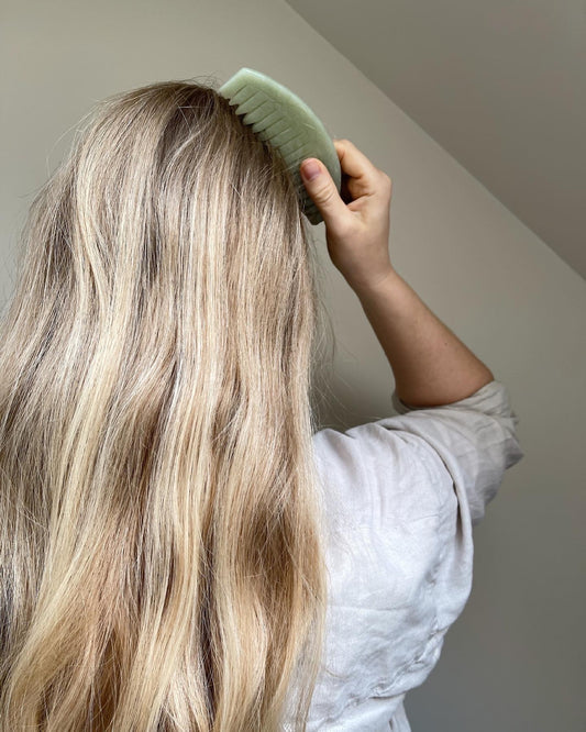 Woman using jade gua sha scalp massage comb for hair growth and relaxation