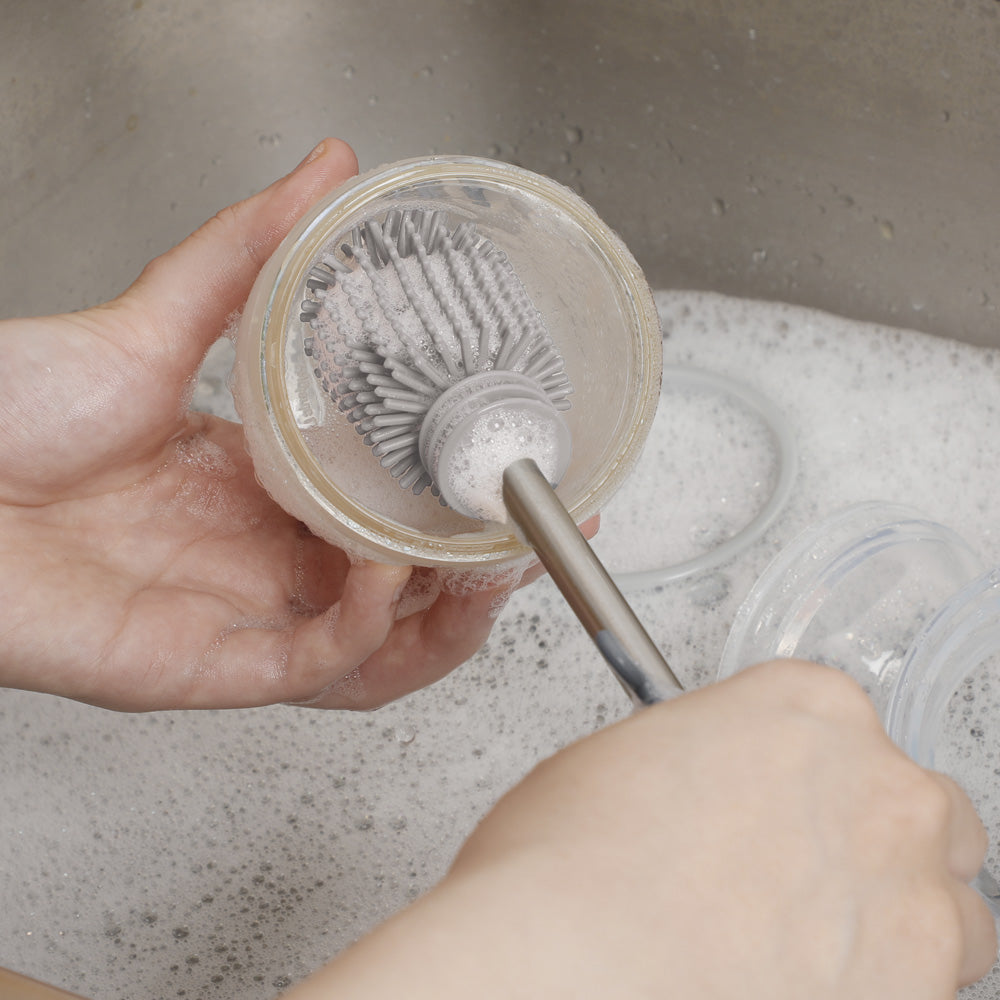 Silicone brush scrubbing inside baby bottle with soapy water in sink