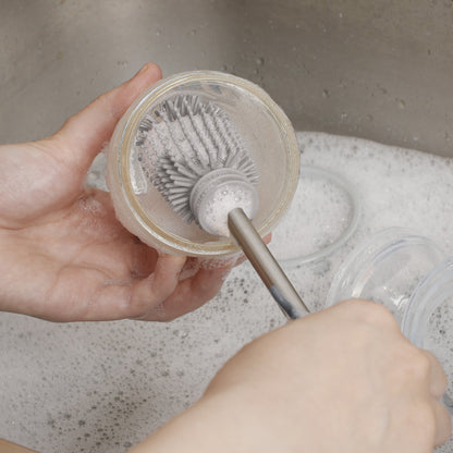 Silicone brush scrubbing inside baby bottle with soapy water in sink