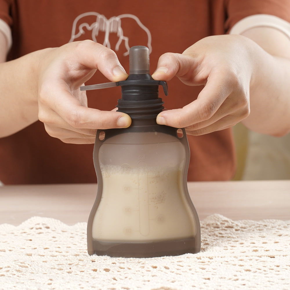 Hands attaching sippy spout to reusable baby food pouch filled with milk for feeding