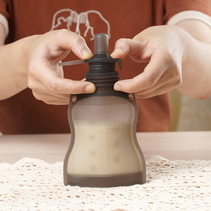 Hands attaching sippy spout to reusable baby food pouch filled with milk for feeding