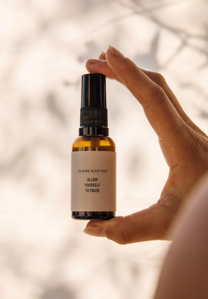The hand holding a bottle of a calming sleep mist by Mama Matters