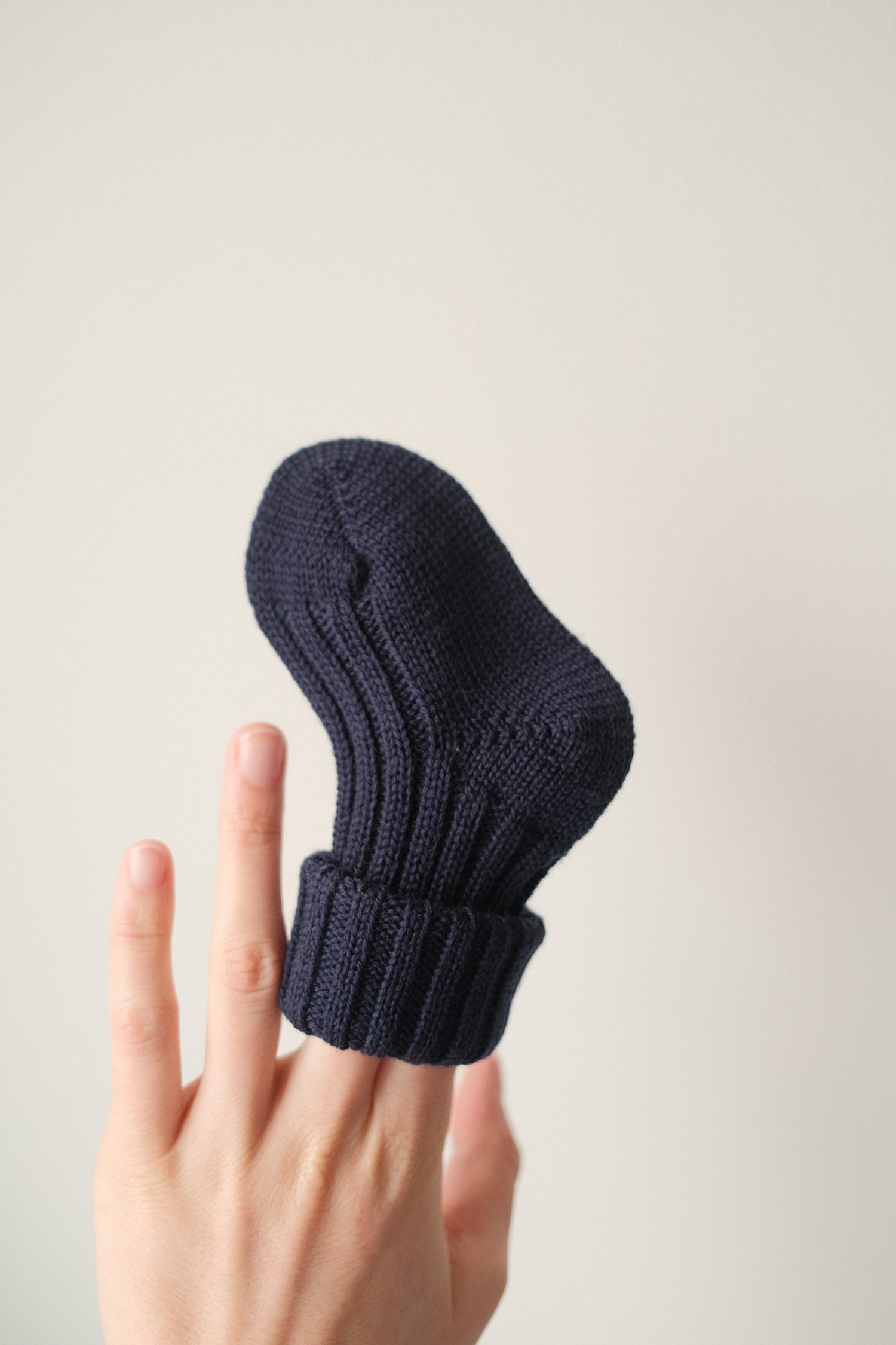 Grödo organic wool baby sock in navy blue held on fingers showing soft knit texture and cozy fit