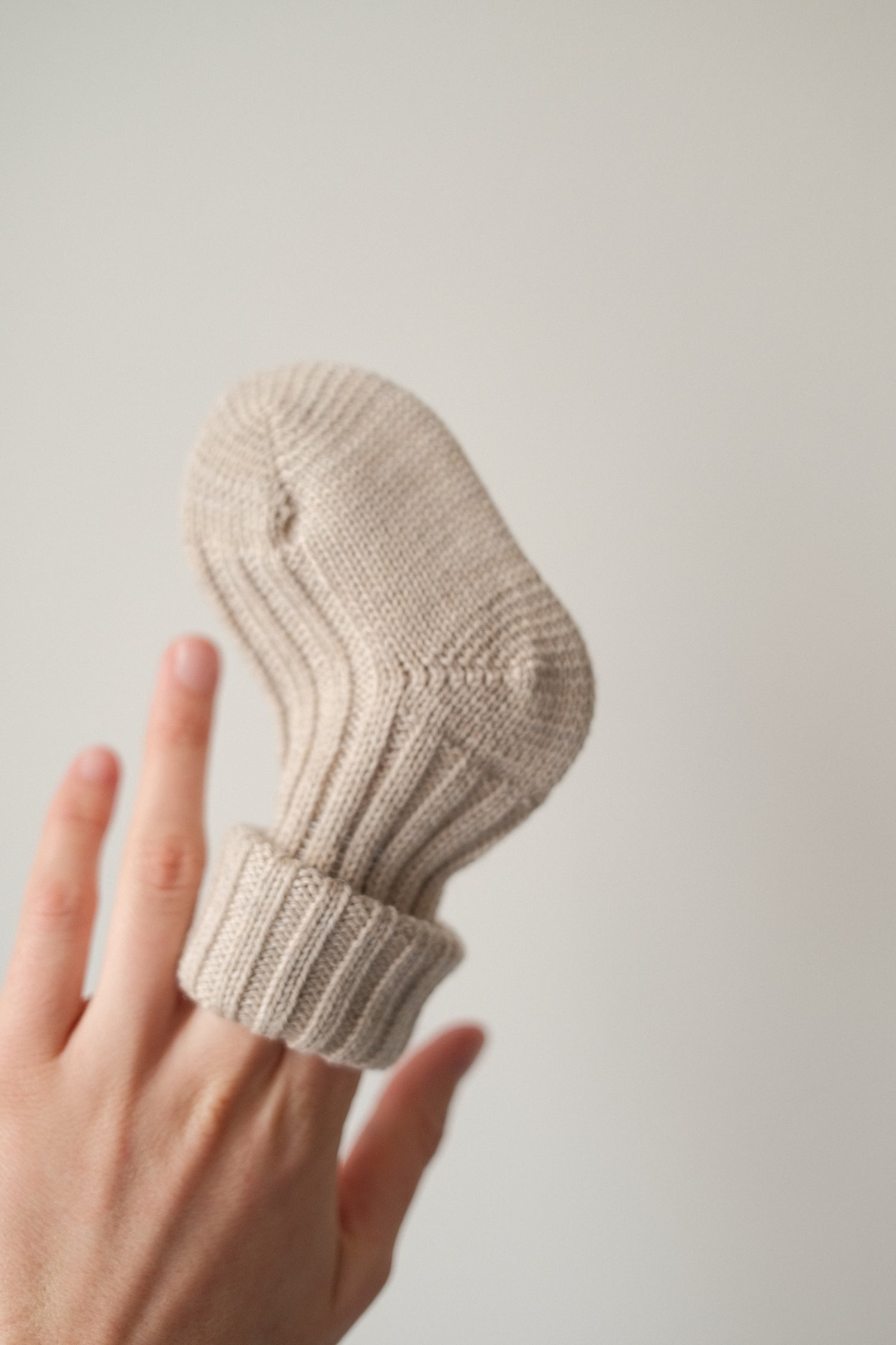 Grödo organic wool baby sock in oat melange on fingers showing warm ribbed cuff and soft knit texture