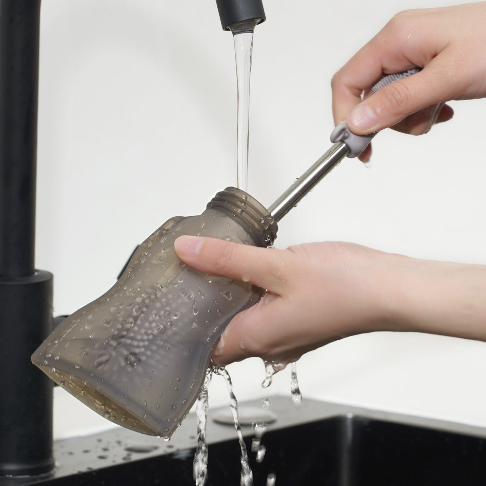 Washing reusable baby food pouch with cleaning brush under tap water for thorough hygiene