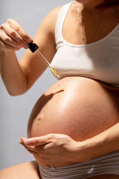 Pregnant woman applying belly oil with dropper to support skin elasticity during pregnancy