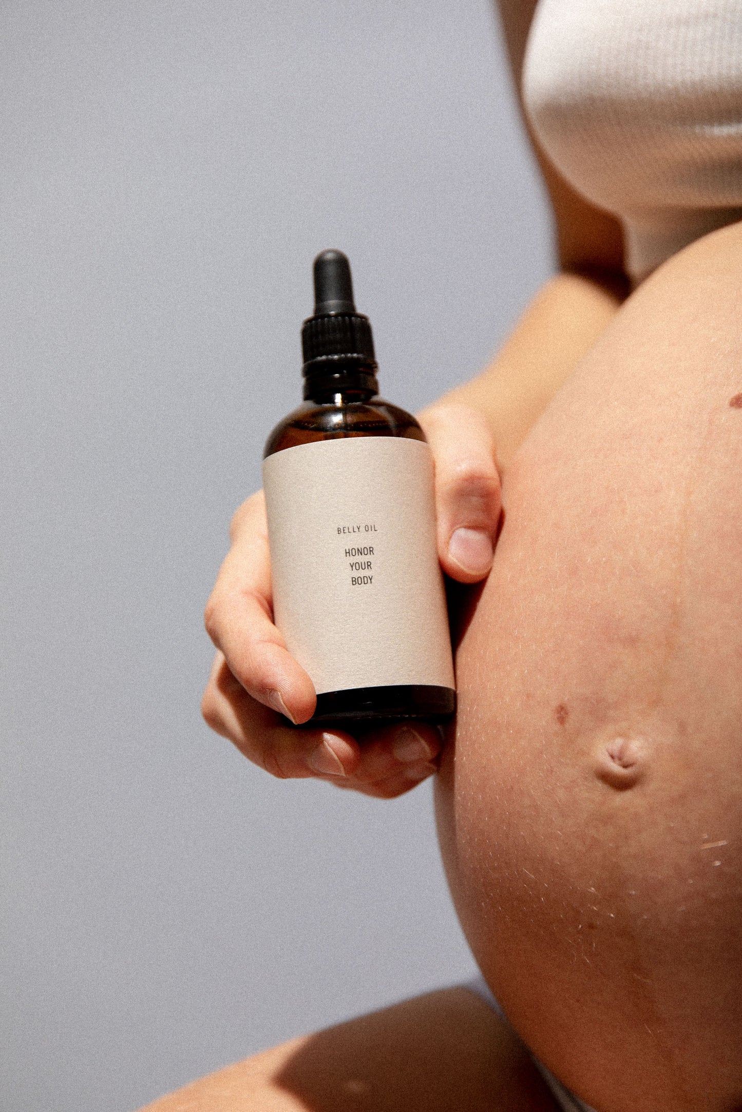 Pregnant woman holding belly oil bottle next to bump showing nourishing pregnancy skincare