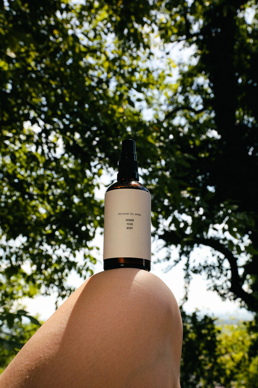 Recovery oil spray bottle balanced on knee outdoors for natural postpartum body care